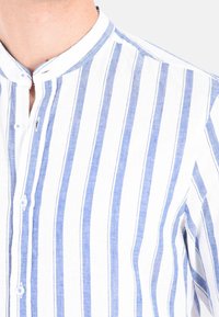 Camicia a maniche corte con bottoni, caratterizzata da righe verticali blu e bianche, colletto alla mandarina e un tessuto leggero con una finitura leggermente testurizzata.