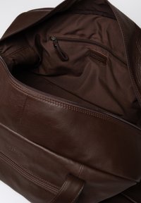 Brown leather handbag with a zip closure. Interior features a smooth fabric lining and a zip pocket. Sturdy handles for easy carrying.