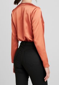 Satin orange långärmad topp med lös passform, matchad med figurnära svarta högmidjade jeans med bakfickor och texturerad tyg.