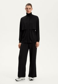 Zwart polyester trainingspak met een cropped top met hoge kraag en een verstelbare taille, gecombineerd met wijde broekspijpen.