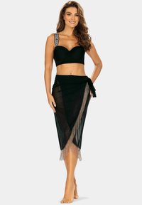 Czarny bikini z dekoracyjnymi białymi paskami; czarna przezroczysta spódnica z frędzlami na końcach. Gładka tekstura i dopasowany krój.