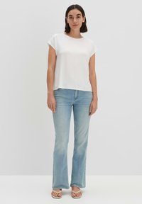 Top bianco a maniche corte abbinato a jeans svasati di colore azzurro chiaro e sandali bassi. Il top presenta una texture liscia e una vestibilità comoda.