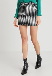 Mini gonna houndstooth bianco e nero con vita alta, dettagli con zip e tessuto testurizzato. Abbinata a stivali neri lucidi alla caviglia.