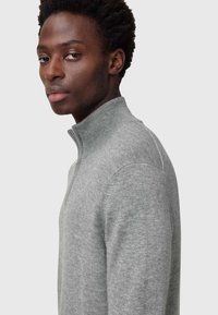 Maglione grigio a maglia con collo alto e zip parziale, caratterizzato da una texture liscia e da un design aderente, mostrato da un angolo laterale.