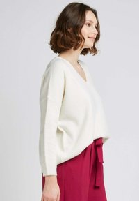 Pull en ivoire surdimensionné avec un col en V, des manches longues et une texture douce, associé à une jupe rose taille haute avec un détail à nouer.