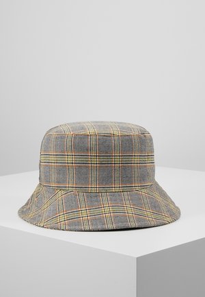 Chapeau seau à carreaux avec un motif quadrillé gris, jaune et orange, présenté sur un socle blanc contre un fond gris clair uni.