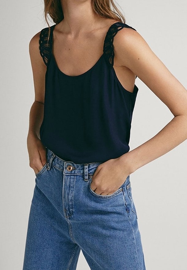 Débardeur bleu marine avec des détails en dentelle sur les bretelles, associé à un jean en denim bleu clair taille haute. Texture lisse.