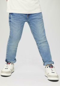 Lichtblauwe denim jeans met een slim fit, voorzien van opgerolde boorden en contrasterende stiksels. Gecombineerd met witte sneakers en marineblauwe accenten.
