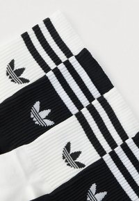 Melnas un baltas svītras zeķes ar ribotu tekstūru un melnu izšūtu logotipu ar svītrām lapas dizainā.