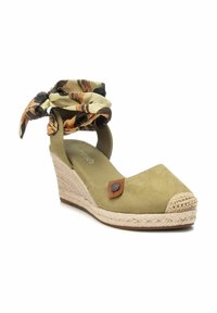 Scarpa con zeppa in suede verde, con suola in juta intrecciata, caratterizzata da un nastro in tessuto decorato e dettagli in pelle marrone.