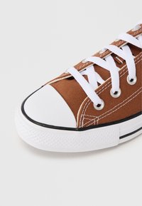 Καφέ καμβαδένιο αθλητικό παπούτσι με λευκά κορ δόνια, λαστιχένιο προστατευτικό στη μύτη και μαύρη επένδυση. Διαθέτει μεταλλικές σιαγόνες και αντίθετες ραφές στο επάνω μέρος.