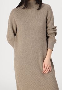 Abito lungo beige a coste con colletto alto e maniche morbide, caratterizzato da una linea dritta e una texture delicata.