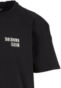 Čierne bavlnené tričko s voľným strihom. Má krátke rukávy a potlačený biely text "TOUCHDOWN SEASON" na ľavej strane.