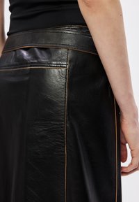 Mustat nahkahame, jossa on sileä pinta, oranssit tikkaukset saumoissa ja litteä vyötärön design.