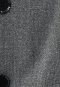 Närbild av grått tyg med två svarta knappar, som visar vävstrukturen och detaljer i plagget.