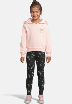 Lys rosa hettegenser med en buegrafikk; svarte leggings med fargerike blomstermønstre; rosa sneakers med rynkede detaljer.