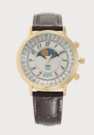 Χρυσό ρολόι Timex quartz με καφέ δερμάτινο λουράκι, λευκό καντράν που δείχνει ώρα, ημερομηνία, ημέρα και ένδειξη φάσεων της σελήνης.