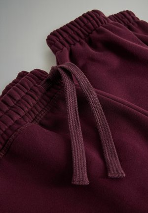 Burgundi spalvos sportinės kelnės su elastingu juosmeniu ir raišteliu. Minkšta medžiaga su ripsuotu detalėmis aplink juosmenį.