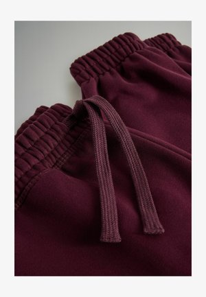 Burgundowe spodnie dresowe z elastycznym pasem i sznurkiem. Miękki materiał z prążkowanymi detalami wzdłuż pasa.