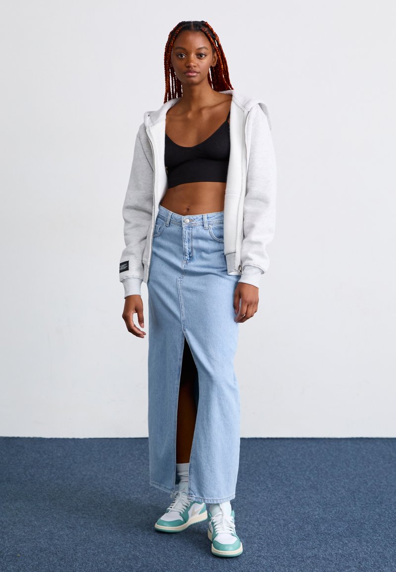 Lys blå denim maxi-skjørt med splitt foran, kombinert med en svart kort topp og en lys grå hettegenser. Brukt med hvite og teal sneakers.