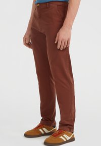 Bruine katoenen chinos met een rechte pasvorm, voorzien van voorzakken en een knoopsluiting. Gecombineerd met bruin-witte sport sneakers.
