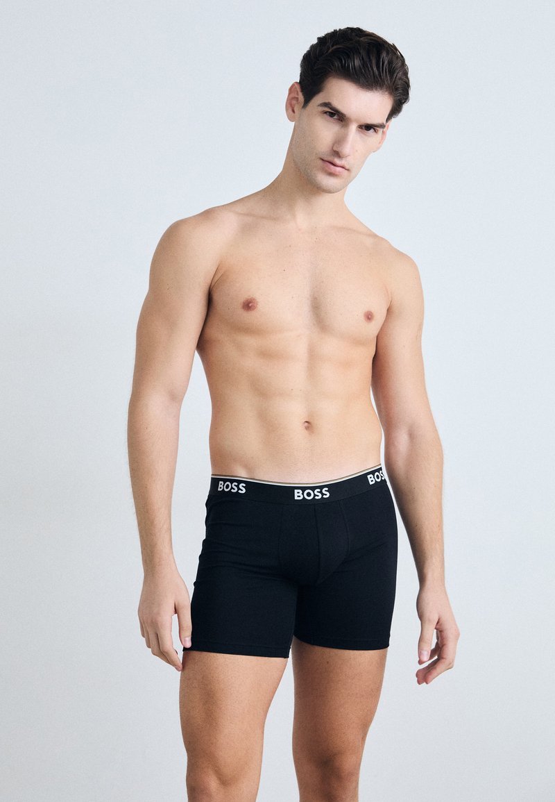 Schwarze Boxershorts mit enger Passform, ausgestattet mit einem weißen Bund, der mit "BOSS" versehen ist. Das Material wirkt glatt und elastisch, ausgelegt für Komfort.