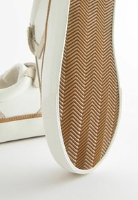 Vit sneaker med en beige mockadekor, rund design och gummisula med fiskbensmönster. Stabil konstruktion med en ren finish.