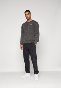Gray sweatshirt with logo, black athletic pants featuring side pockets, and white sneakers. Smooth texture, casual design, and relaxed fit.