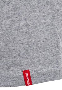 Harmaa puuvillakangasta t-paita, jossa on punainen lappu helman lähellä ja "hummel"-logo. Pehmeä rakenne ja heather-kuvio.