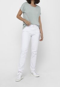 Camiseta a rayas verde y blanca, corte relajado, combinada con jeans blancos y zapatillas grises y blancas. Textura suave, sin patrones visibles en los pantalones.