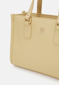 Gul syntetisk håndveske med strukturert form, gyllen logoaksent og to topphåndtak. Har horisontal søm og subtil tekstur.