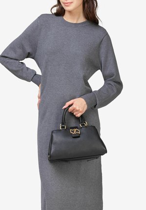 Black leather handbag with a structured shape, gold hardware, and a top handle, held by a person wearing a gray knit dress.