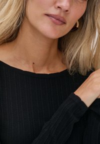 Schwarzer gestrickter Pullover mit gerippter Textur, weitem Boot-Ausschnitt und langen Ärmeln. Nahaufnahme, die den Ausschnitt und die Hand des Models zeigt.