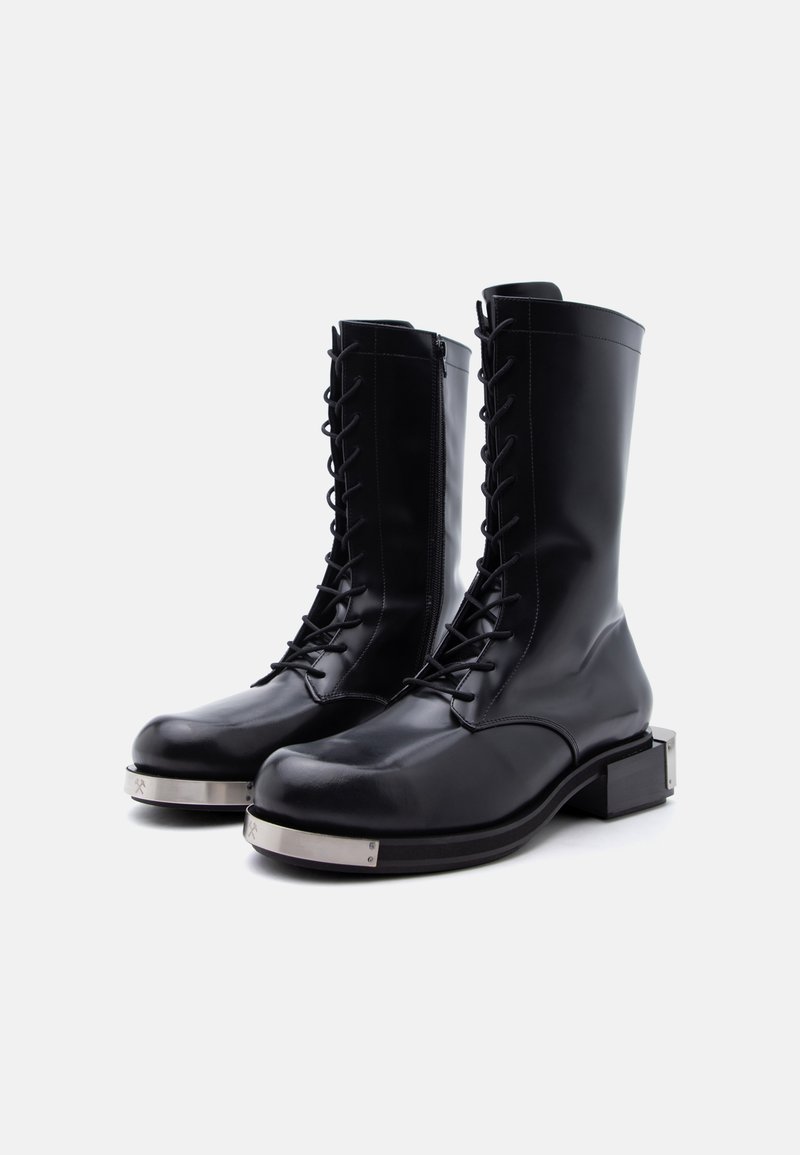 Black mid-calf leather boots with front laces, side zippers, chunky heels, and silver metal plates on the toe caps.