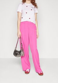 Camiseta de manga corta, a rayas rosas con motivos de corazones rojos, combinada con pantalones rosados de pierna ancha y cintura alta. Bolso plateado y calzado colorido.