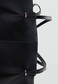 Bolso de mano de cuero negro con textura suave, forma definida, base plana y detalles en tono dorado. Presenta dos asas ajustables.