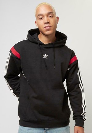 Crna pamučna dukserica s dugim rukavima, s crvenim i bijelim akcentnim prugama, prednjim kenguruh džepom i Adidas logotipom na prsima.