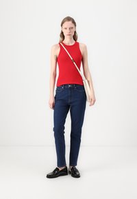 Rød ribbet ermeløs topp parret med mørkeblå jeans og svarte loafers, accessorized med en kremfarget crossbody-veske. Nøytral bakgrunn.