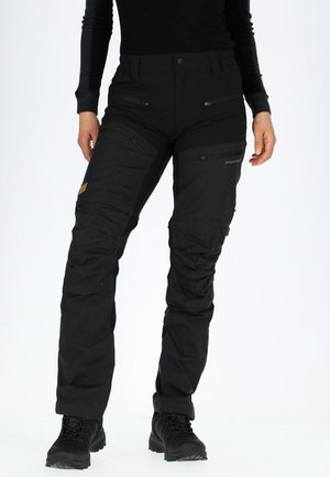 Black waterproof trousers with multiple zippered pockets. Smooth texture, tapered fit with reinforced knees, cuffed hems, and logo detail.