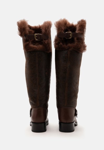 Bottes hautes en cuir brun foncé avec bordure en fourrure en haut et boucles réglables autour des mollets, vues de dos sur fond blanc.