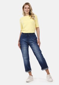 Pantalones jogger de mezclilla con cinturilla elástica, puños enrollados y una textura suave, combinados con una camiseta ceñida de color amarillo brillante.