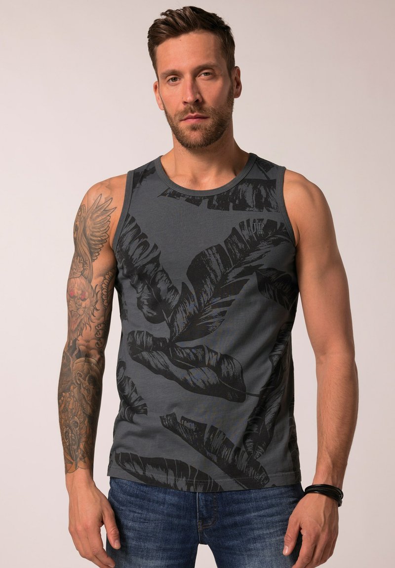 Šedý top bez rukávů s černým vzorem listů; vyrobeno z měkké tkaniny. Nosený s modrými džíny, které ukazují uvolněný střih.