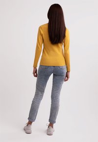 Gul långärmad topp kombinerad med ljusblå denimjeans. Jeansen har upprullade fång och är figursydda, kompletterade med vita sneakers.