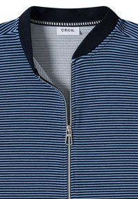 Veste zippée rayée bleu marine et bleu clair. Comprend un col côtelé, une fermeture éclair métallique et un tissu texturé. Étiquette de la marque : CECIL.