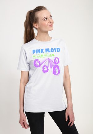 Ung kvinde med hestehale iført hvid Pink Floyd t-shirt med bandmedlemmers lilla ansigter og blågrøn tekst, der kigger op mod højre.