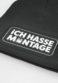 Black knitted beanie with a white patch reading "ICH HASSE MONTAGE" and a small cartoon penguin wearing glasses.
