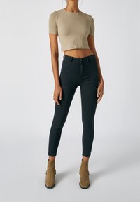 Vaqueros negros ajustados de cintura alta con una textura suave, combinados con una camiseta recortada de algodón de color beige de canalé y botines marrones claros.