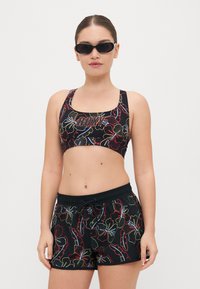 Svart atletisk crop-top og shorts med et blomstermønster i rødt, blått og grønt. Toppen har "ROXY"-logoen. Glatt tekstur.