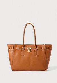 Tan leather tote bag with dual top handles, gold-tone hardware, and a flat-base design. Features decorative stitching and a lock accent.