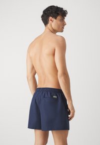 Shorts de bain marine avec taille élastique, poche arrière et accent de logo vert. Tissu léger, coupe ample et longueur au-dessus du genou.